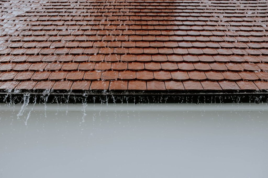 Offerings Brown roof tiles with rainwater cascading down, showcasing architectural texture and detail.